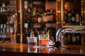 A bar counter with a glass of amber-colored drink garnished with a sprig of rosemary, a crystal decanter, and a bottle of liquor. - Best Western Plus Delta Park Hotel (Mannheim)