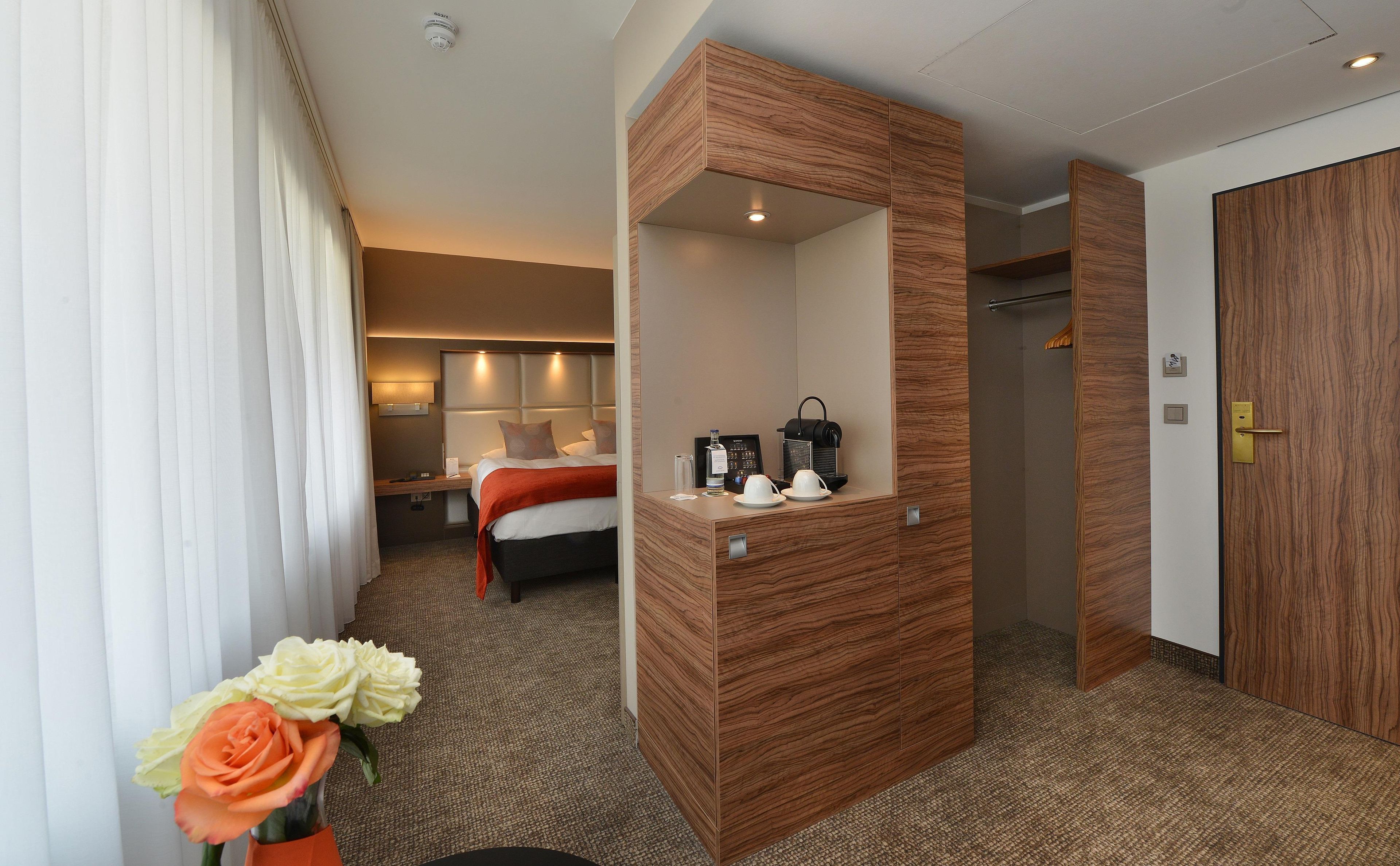 A hotel room with a bed, bedside table, mirror, and a wooden wardrobe.