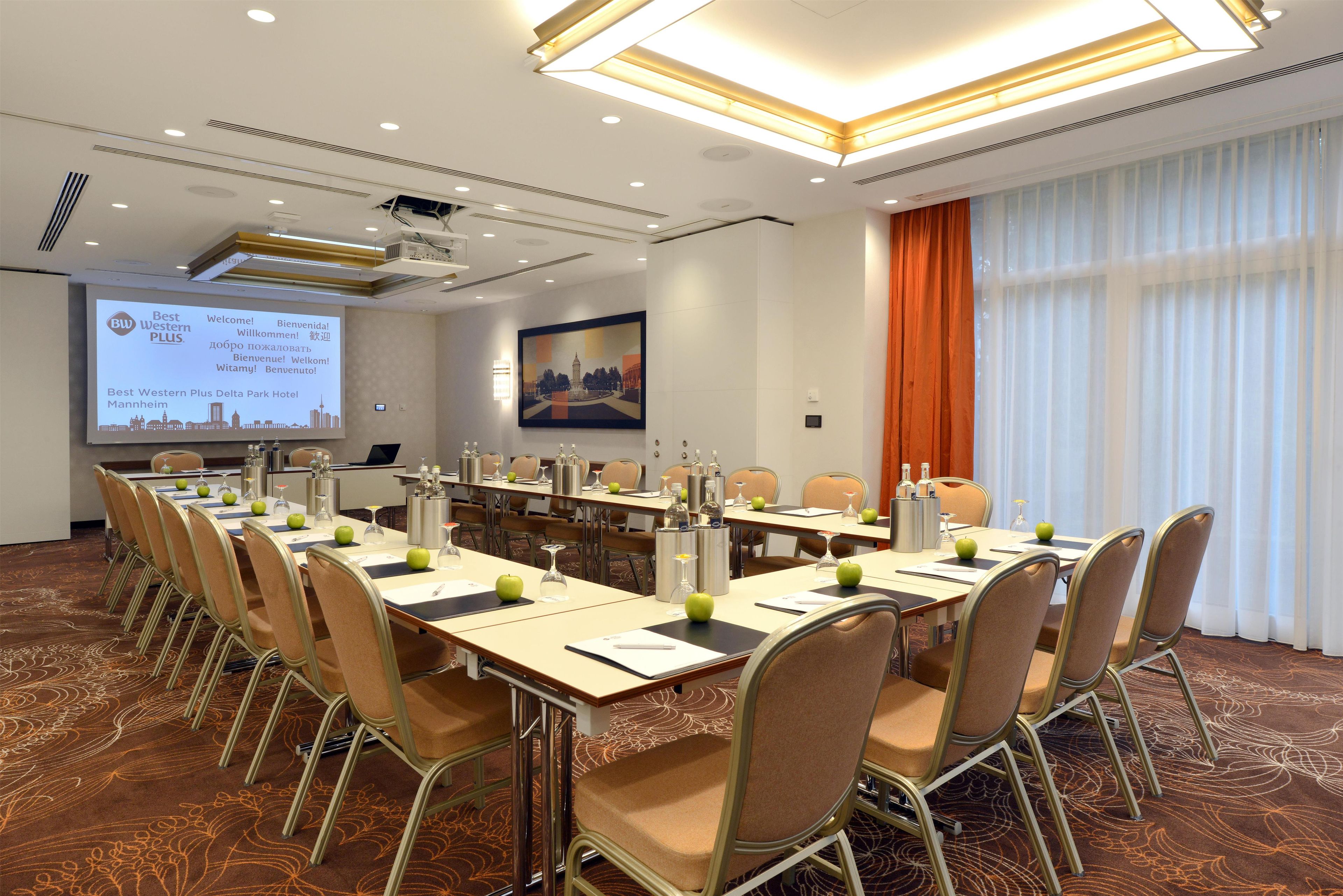 Sala de conferência com uma mesa grande, cadeiras, tela de projetor e um quadro de grande porte na parede.