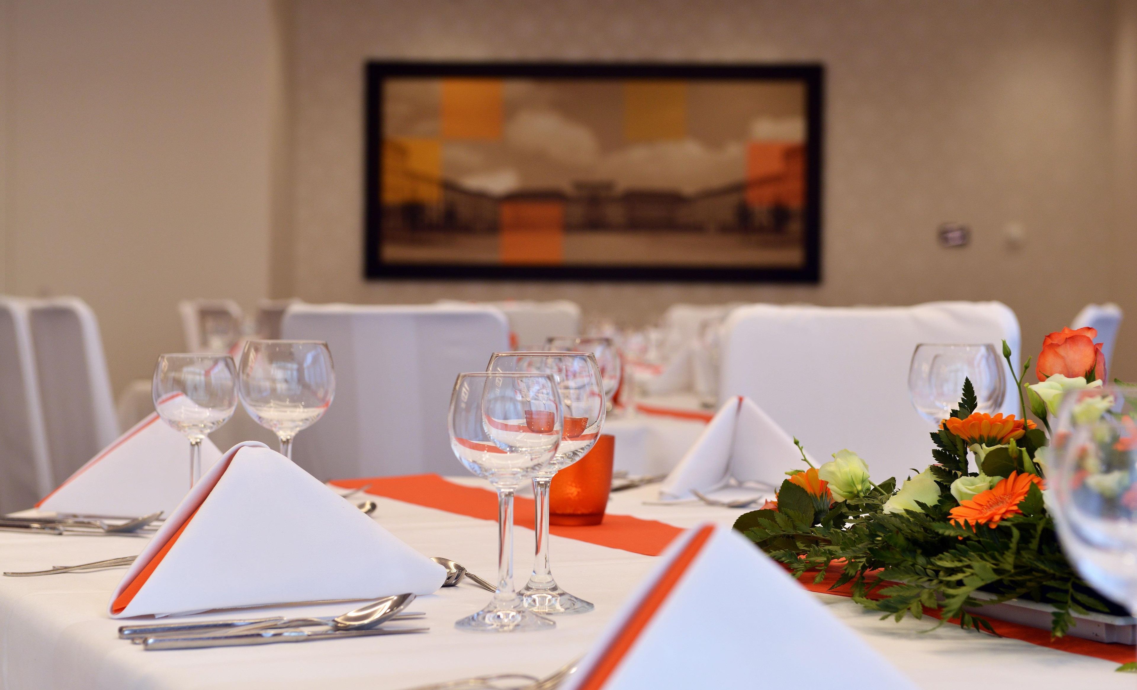 A dining table set with white tablecloths, orange napkins, and clear glassware.