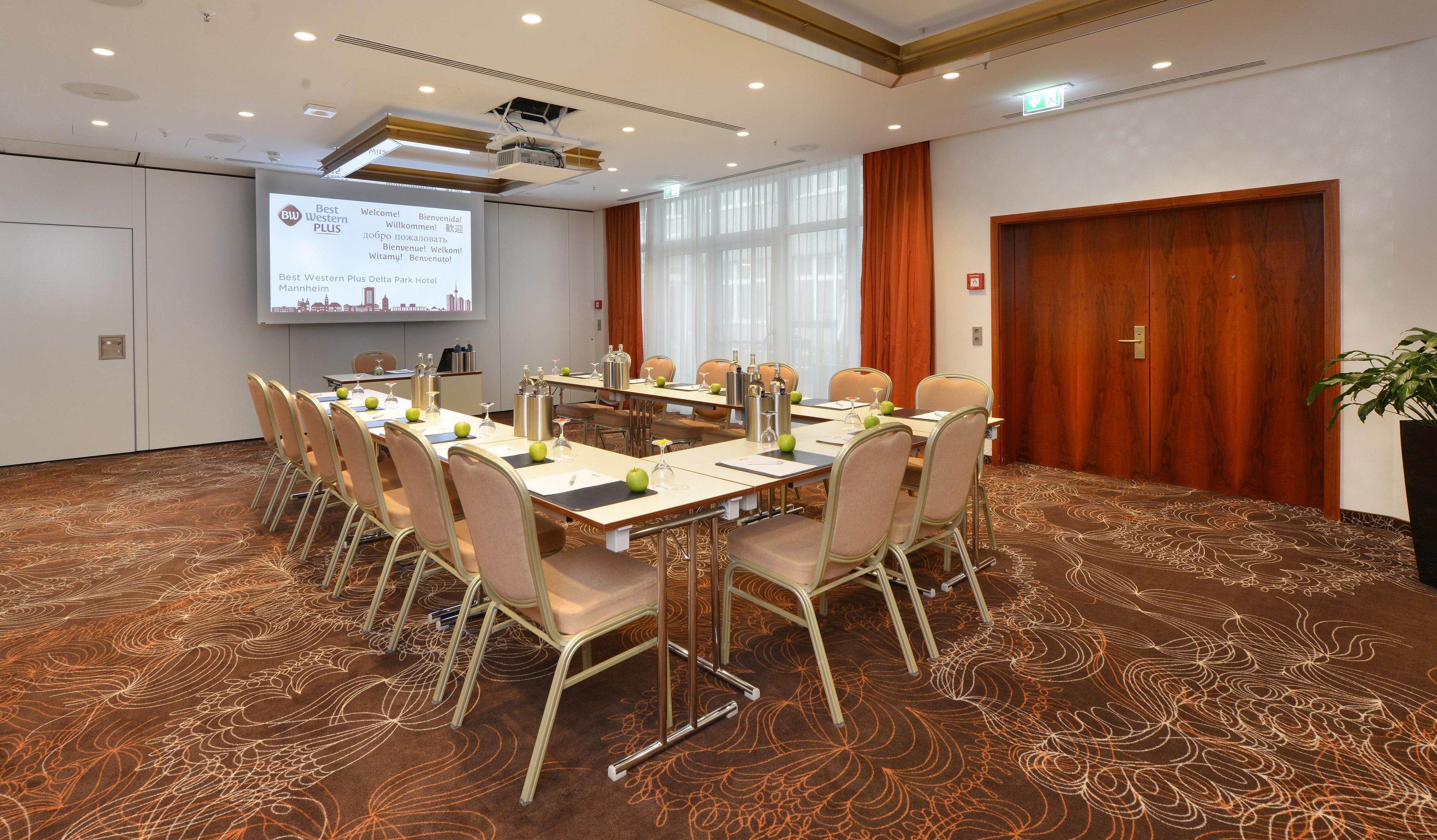 Ein Konferenzraum mit einem großen Tisch, Stühlen, einer Projektionsleinwand und einer Präsentation zum Best Western Plus Delta Park Hotel.