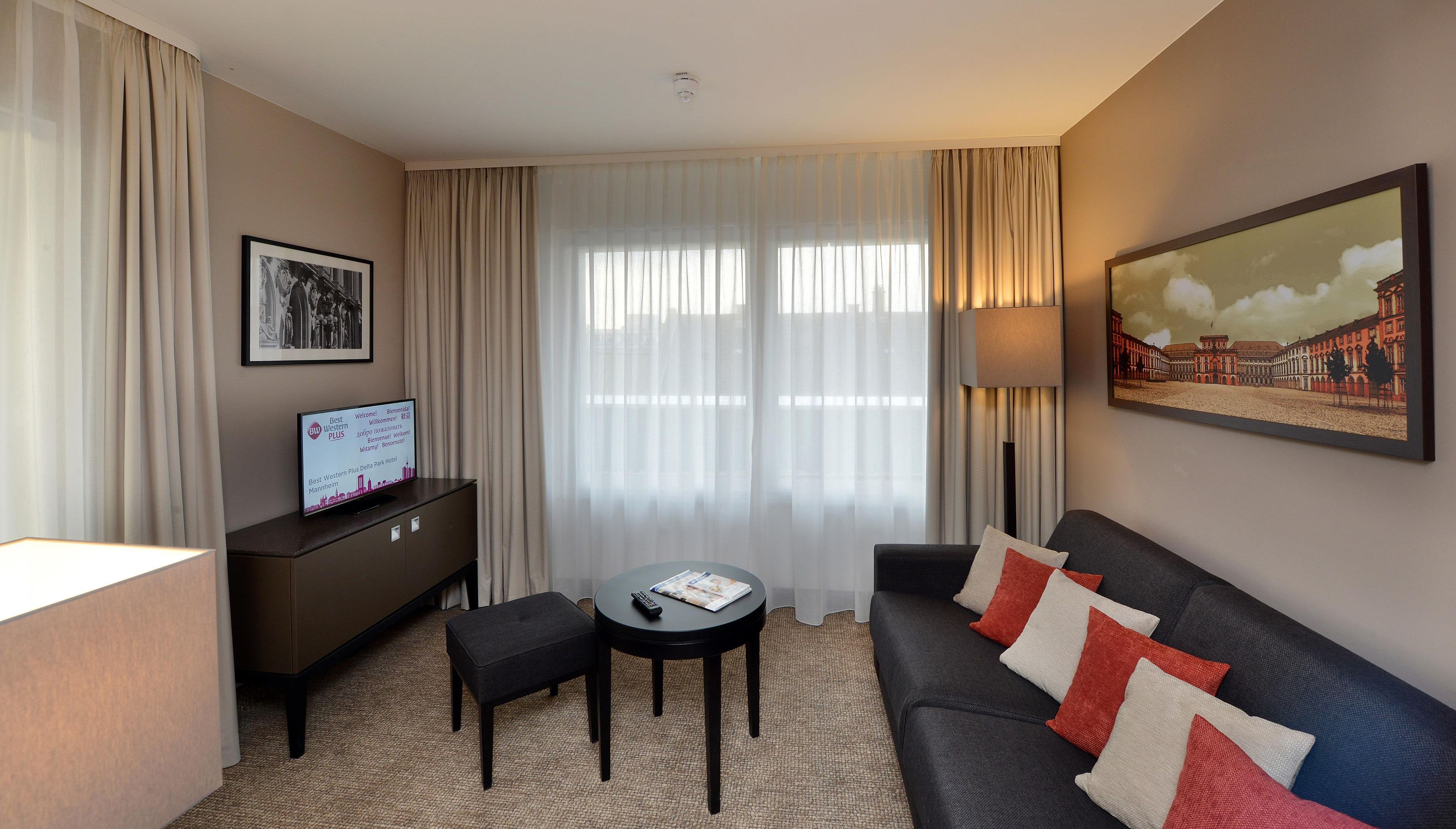 A hotel room with a sofa, a small table, a remote control, a magazine, a framed picture, and a sign with hotel information.