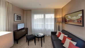 A hotel room with a sofa, a small table, a remote control, a magazine, a framed picture, and a sign with hotel information.