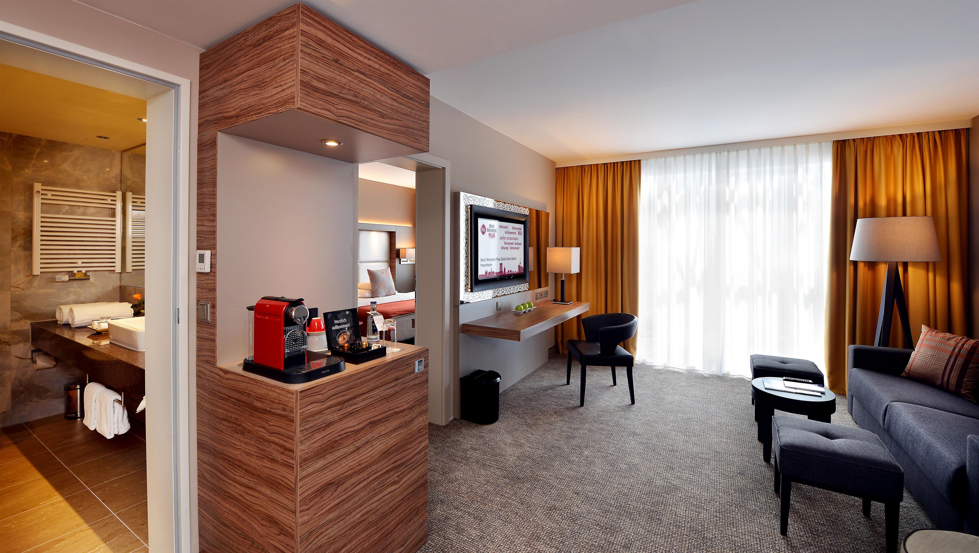 Ein Hotelzimmer mit Sitzgelegenheit, Fernseher, Kaffeeautomat und Schreibtisch.