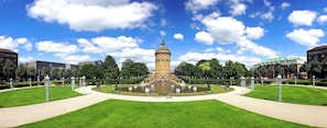 A historic tower with a fountain in the center, surrounded by well-manicured lawns and trees.