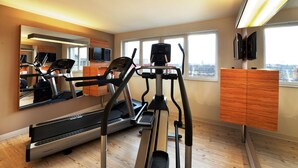 A gym with cardio equipment, a television, and a city view. - Best Western Plus Delta Park Hotel (Mannheim)