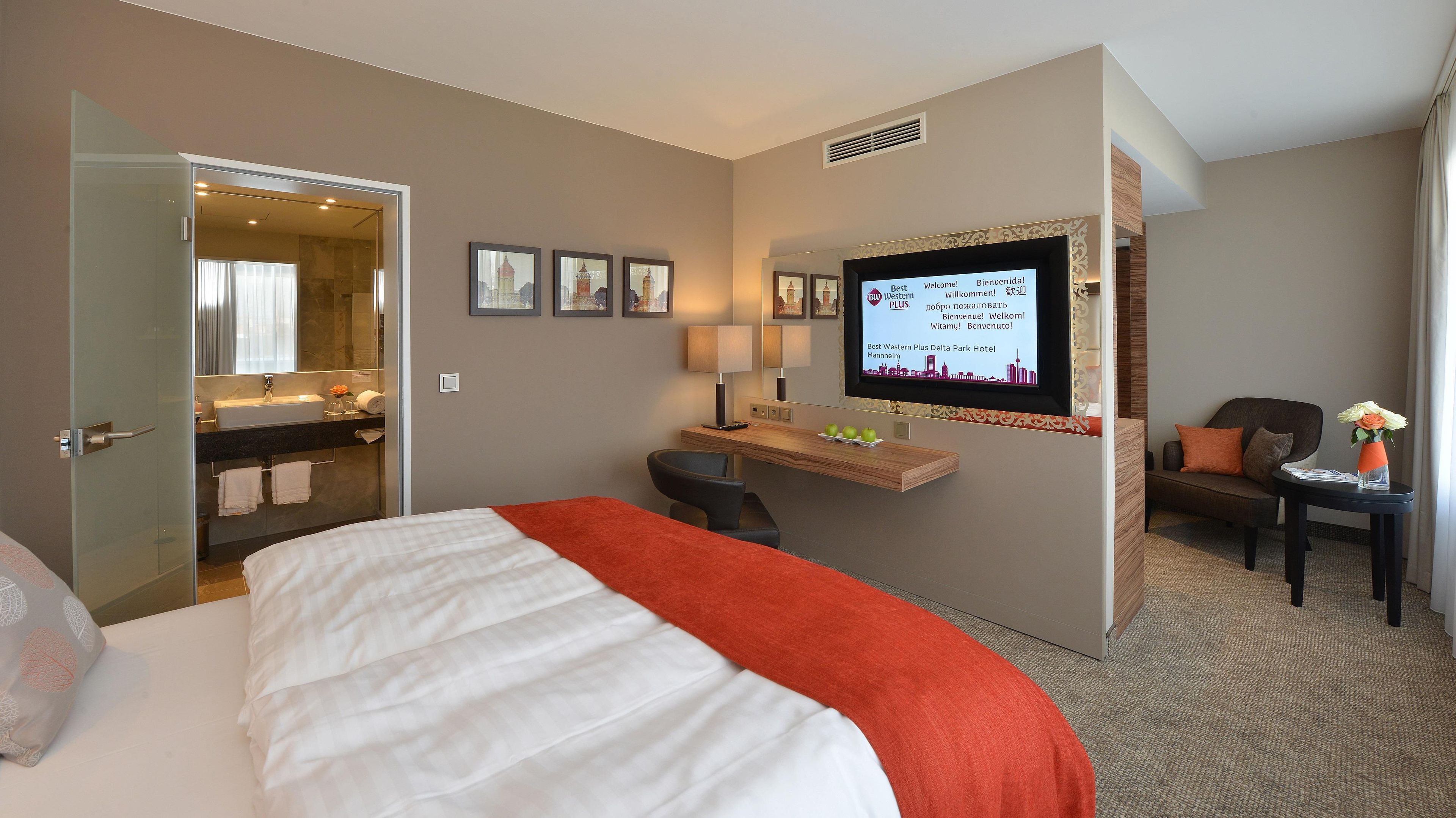 Een hotelkamer met een bed, een bureau, een stoel, een televisie en een badkamer die door een open deur zichtbaar is.