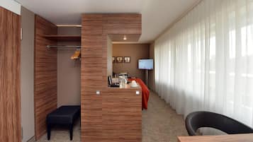 Ein Hotelzimmer mit einem Holzschrank, einem Schreibtisch mit Kaffeemaschine, einem Fernseher und einem Fenster mit Vorhängen.