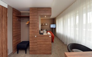 A hotel room with a wooden wardrobe, a desk with a coffee maker, a TV, and a window with curtains. - Best Western Plus Delta Park Hotel (Mannheim)