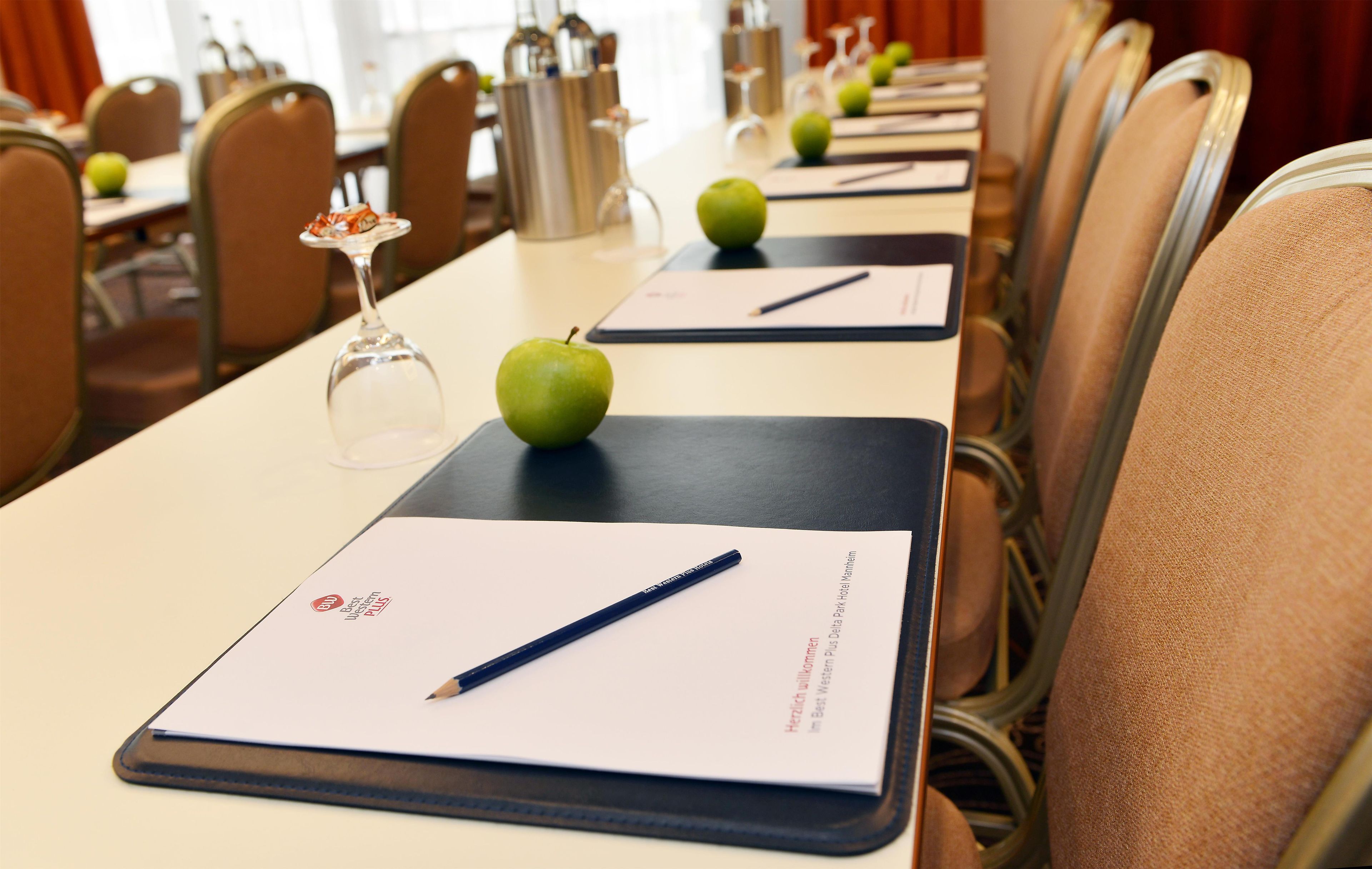 A conference room with a long table, chairs, a wine glass, and an apple on a notepad.
