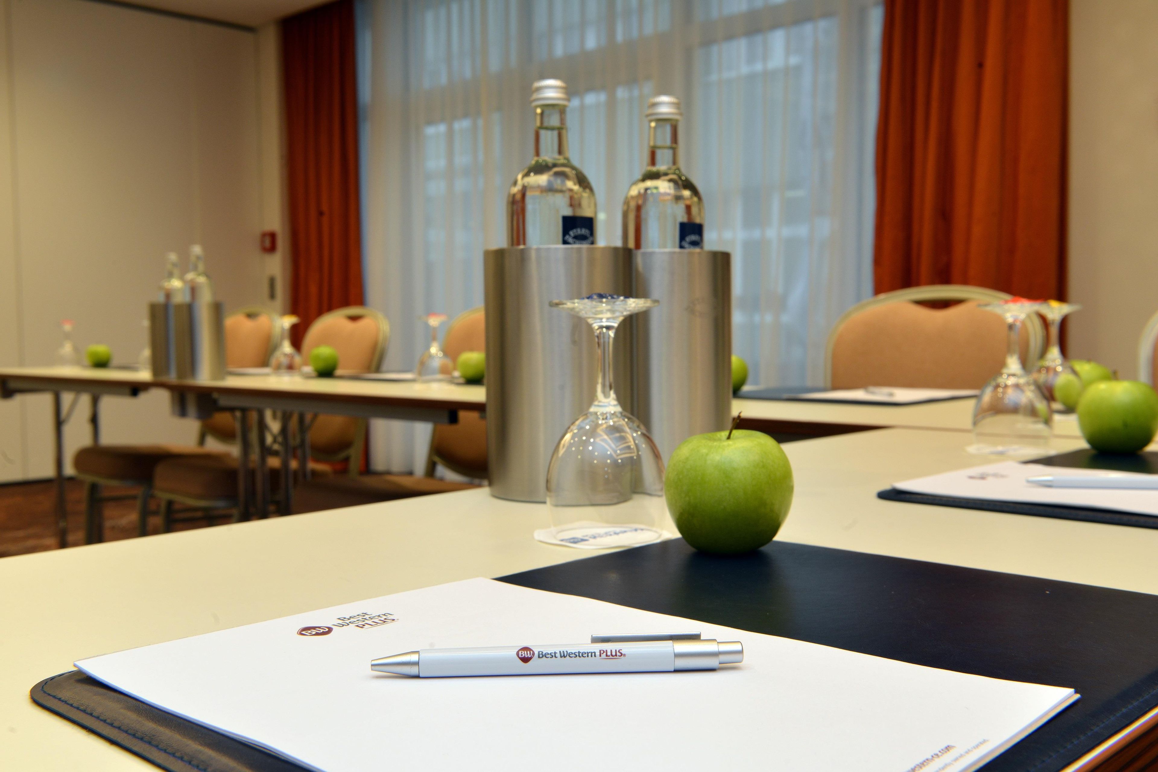 Una sala de conferències amb una taula preparada per a una reunió, que inclou una ploma, un got i una poma.