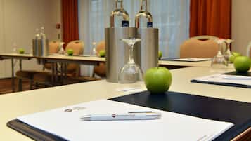 Une salle de conférence avec une table préparée pour une réunion, sur laquelle on trouve un stylo, un verre et une pomme.