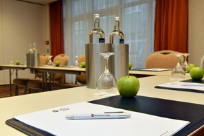 Un salón de conferencias con una mesa lista para una reunión, que incluye una pluma, un vaso y una manzana.