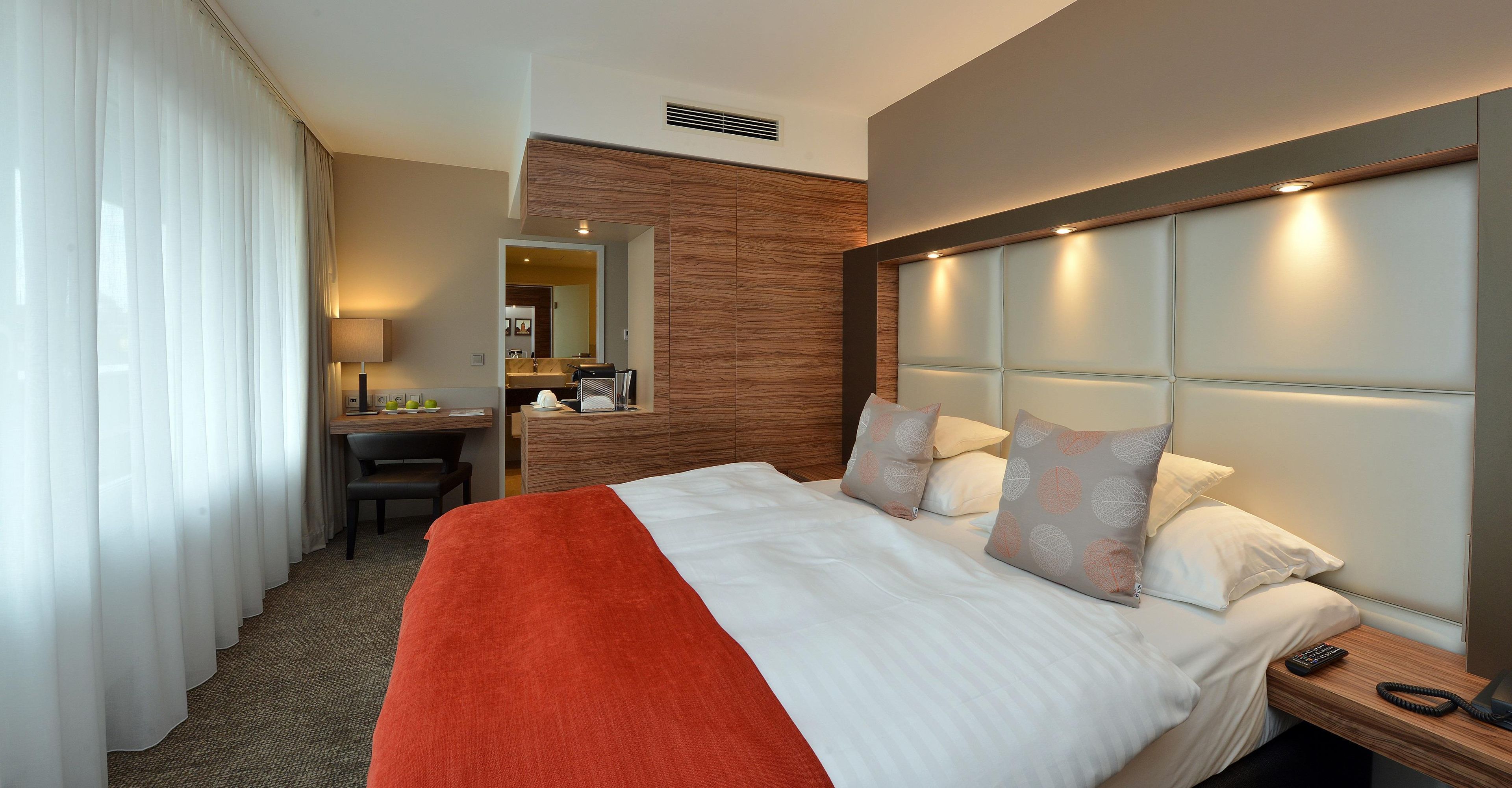A hotel room with a bed, a desk, a chair, and a bathroom visible through an open door.