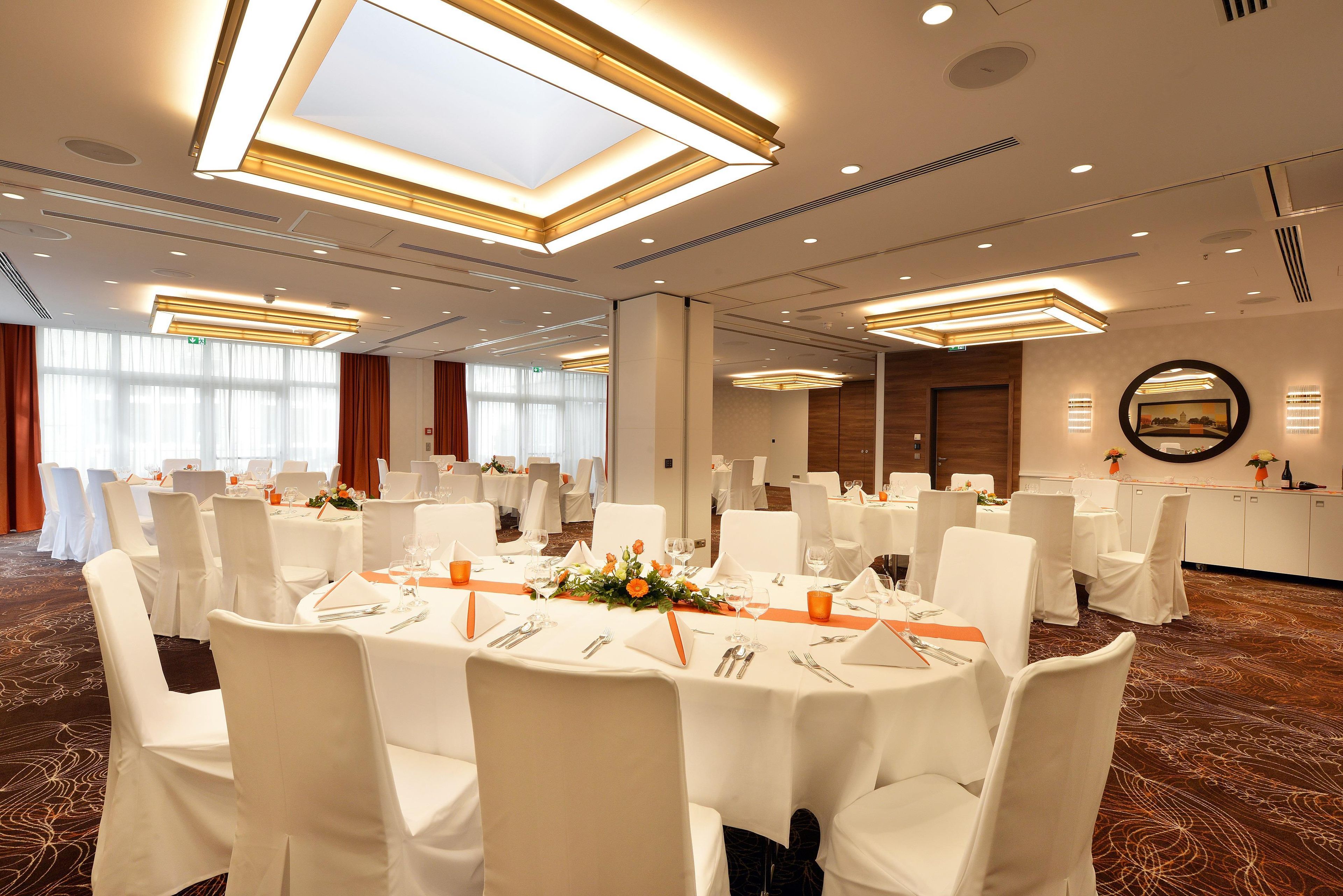 A banquet hall with round tables, white tablecloths, and orange centerpieces.