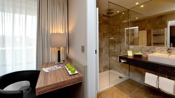 Ein Hotelzimmer mit einem Holztisch, einer Lampe, einer Glasdusche und einem großen Spiegel.