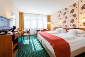 A hotel room with a bed, a desk, a chair, a television, and a window with curtains.