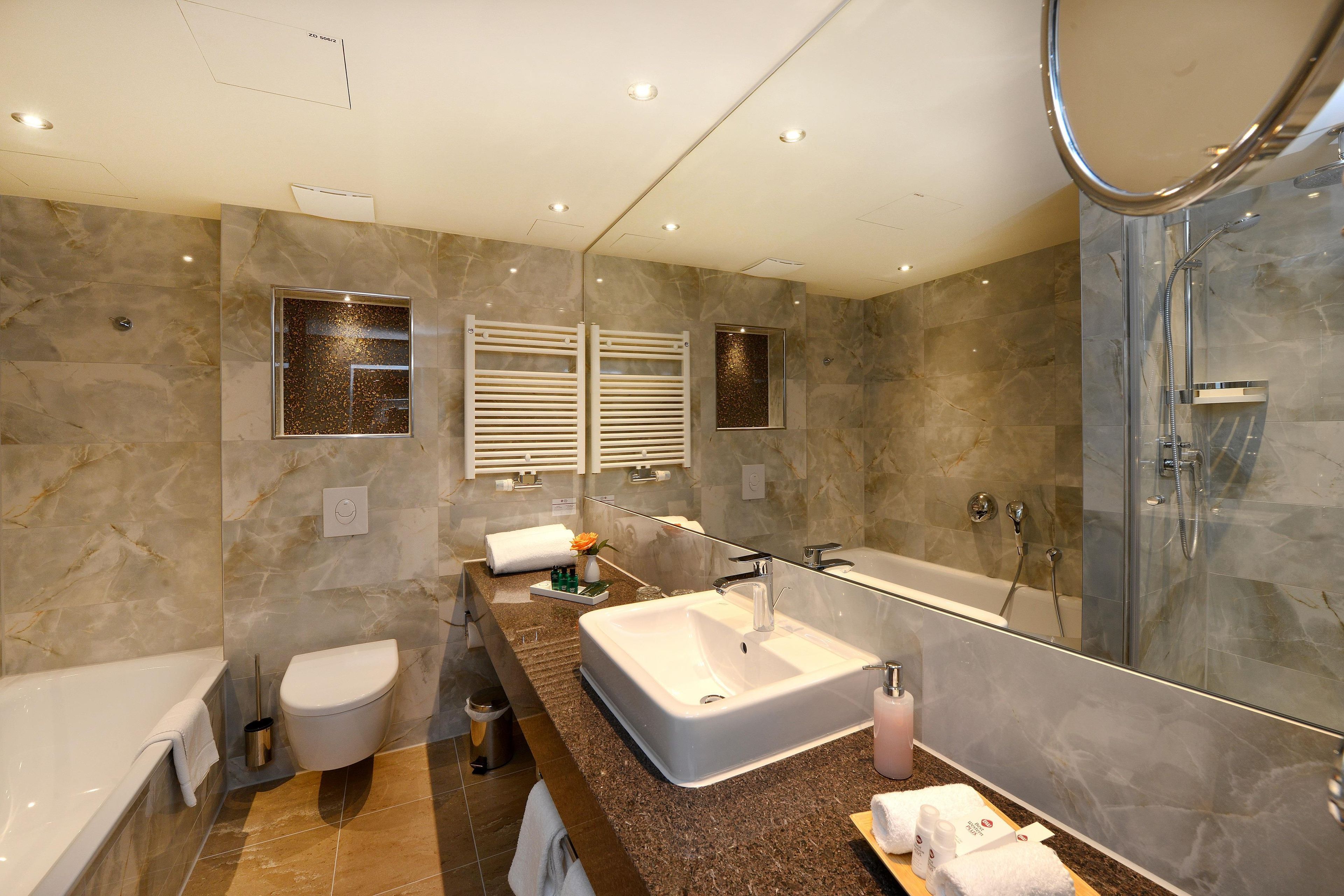A modern bathroom with a large mirror, a bathtub, a toilet, and a shower.