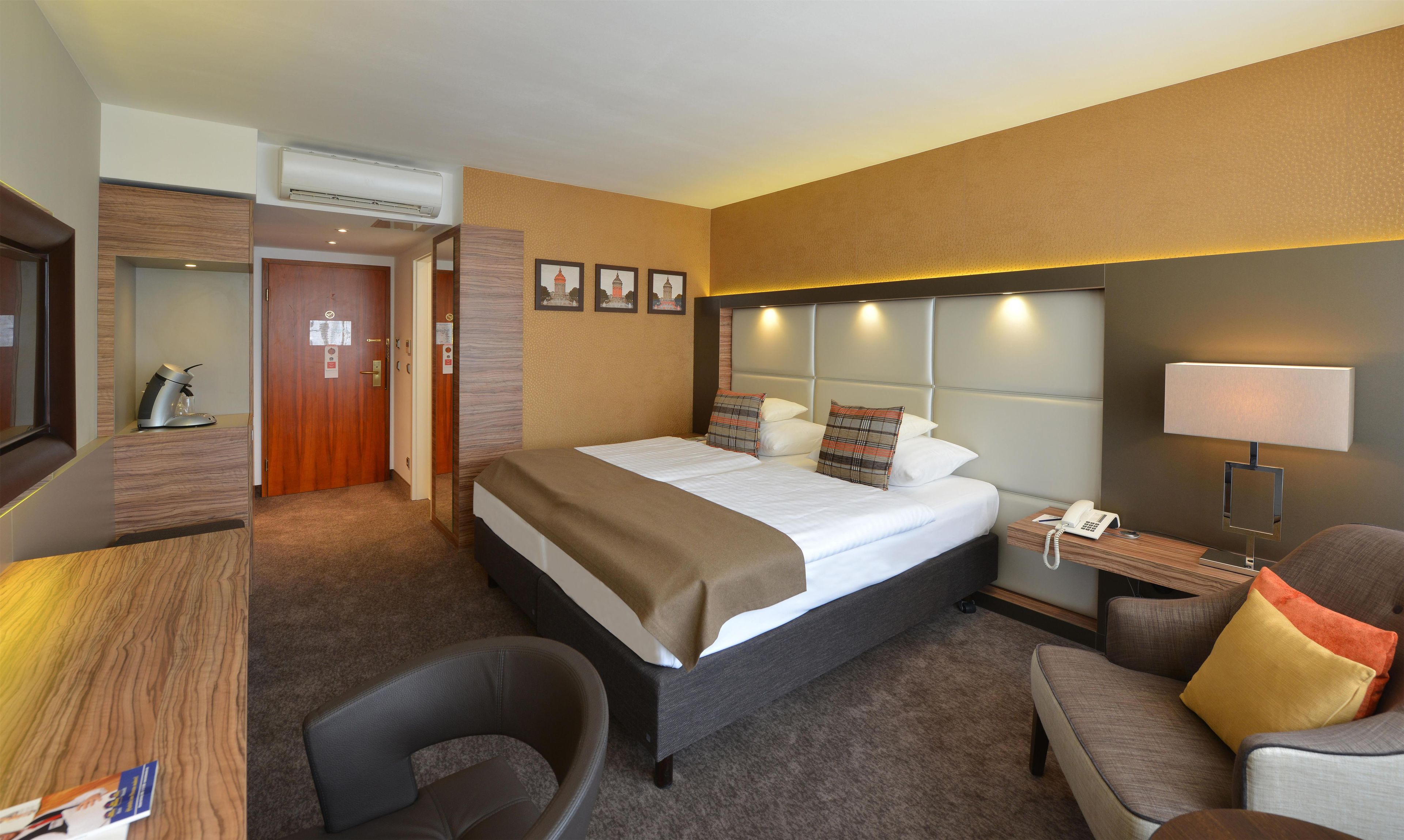 A hotel room with a bed, a desk, a chair, a bedside table with a lamp, and a phone.