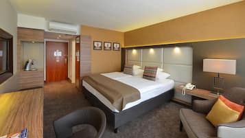 A hotel room with a bed, a desk, a chair, a bedside table with a lamp, and a phone.