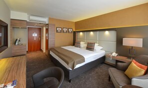 A hotel room with a bed, a desk, a chair, a bedside table with a lamp, and a phone. - Best Western Plus Delta Park Hotel (Mannheim)