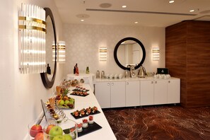 A hotel reception area with a white reception desk, a large mirror, and a buffet with various food items. - Best Western Plus Delta Park Hotel (Mannheim)