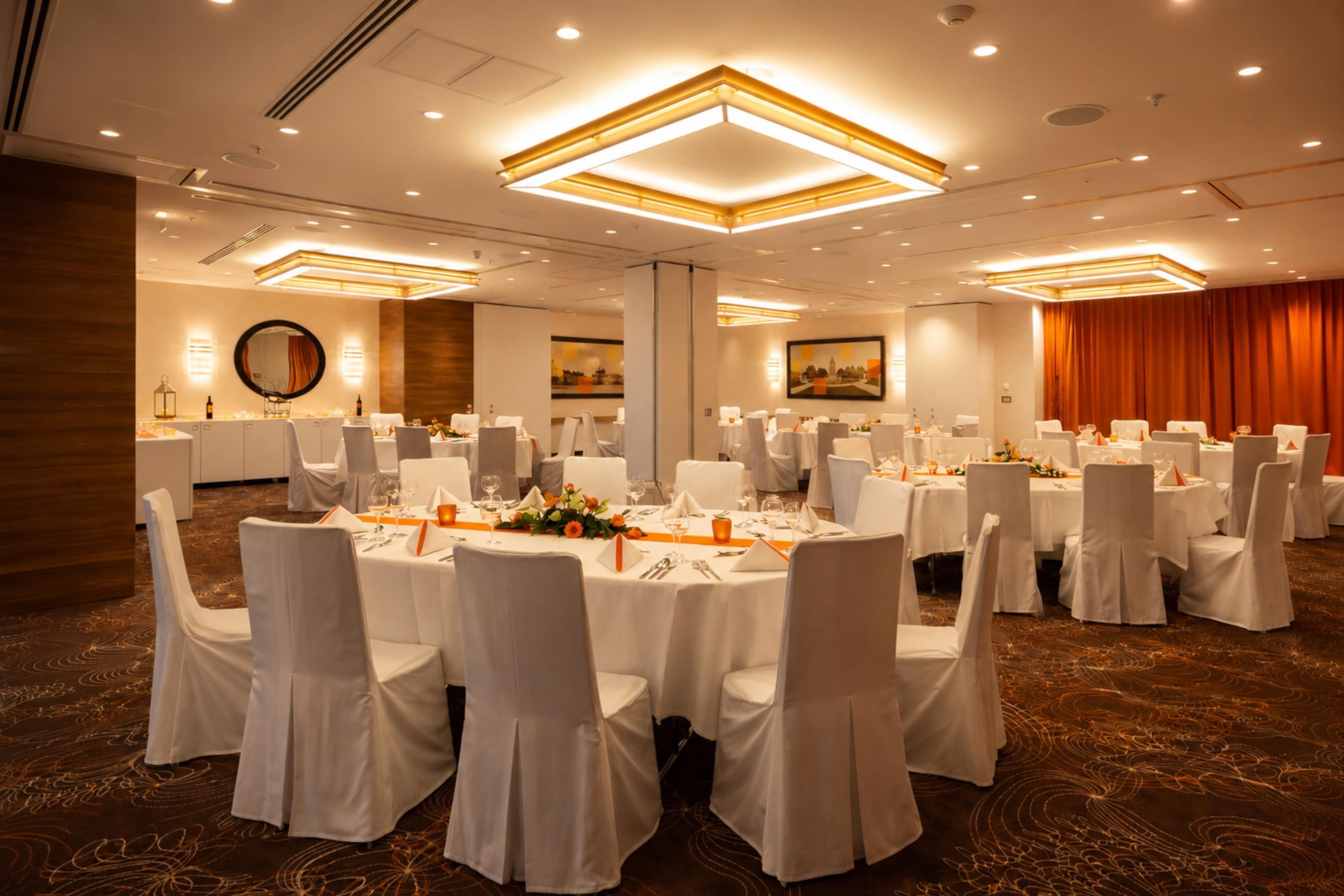 A banquet hall with round tables, white chairs, and a carpeted floor.