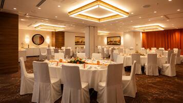 A banquet hall with round tables, white chairs, and a carpeted floor.