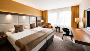 A hotel room with two beds, a desk, a chair, a small table, and a television. - Best Western Plus Delta Park Hotel (Mannheim)