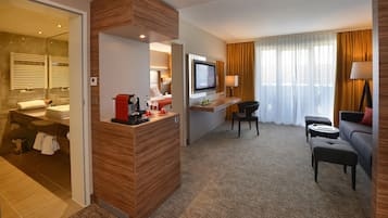 A hotel room with a bathroom, a seating area, and a TV.