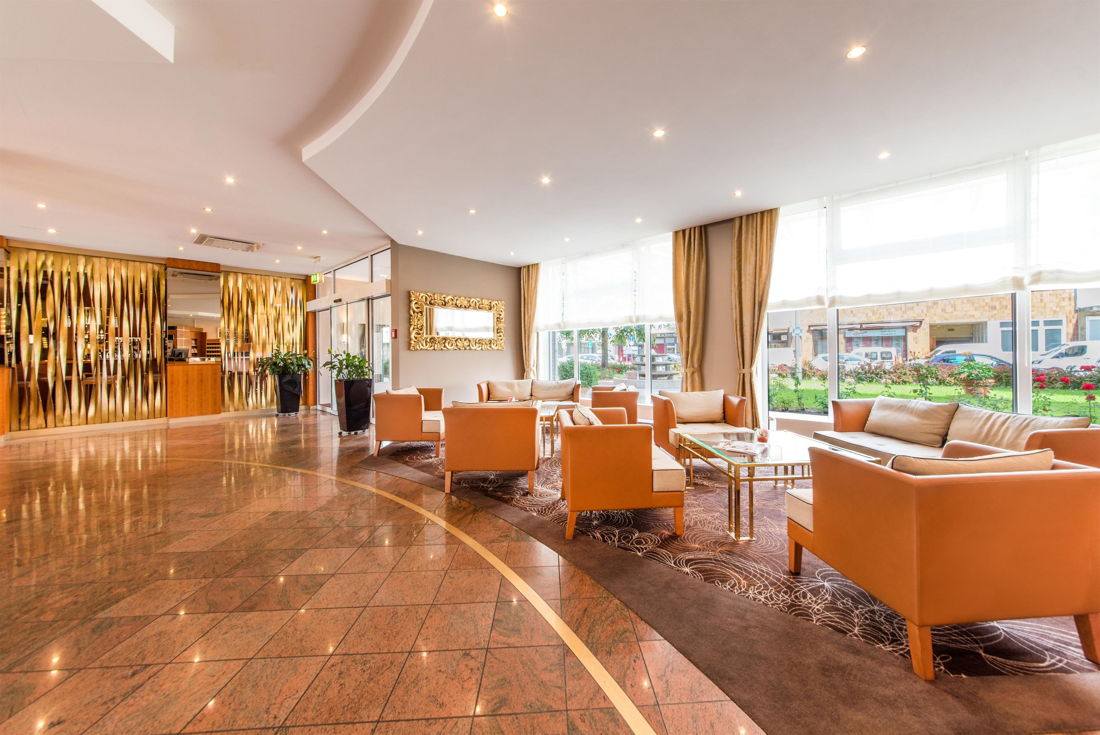 Eine geräumige Lobby mit einer Rezeption, einer Sitzecke und großen Fenstern mit Blick ins Freie.