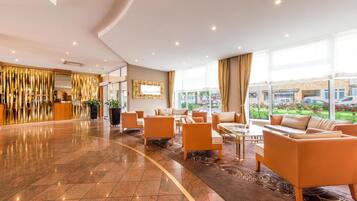 Eine geräumige Lobby mit einer Rezeption, einer Sitzecke und großen Fenstern mit Blick ins Freie.