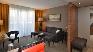 A hotel room with a sofa, armchairs, a small table, a lamp, and a painting on the wall. - Best Western Plus Delta Park Hotel (Mannheim)