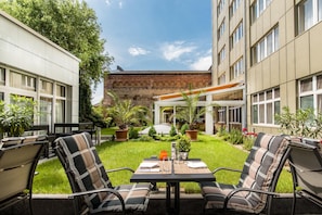 A courtyard with outdoor seating, a brick building, and greenery.
