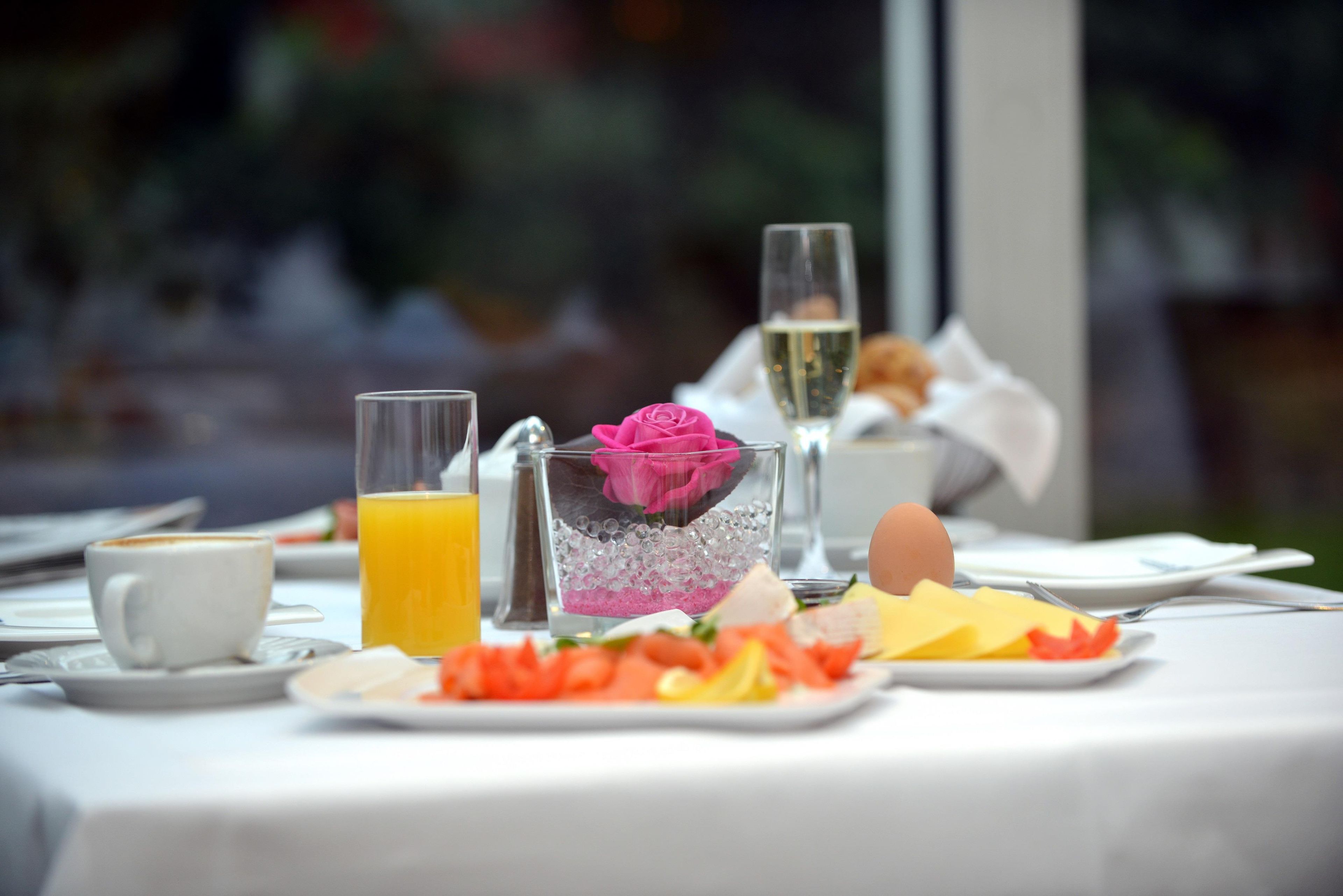 A breakfast setting with a glass of orange juice, a glass of white wine, a plate with eggs, cheese, and vegetables, and a pink flower in a glass.