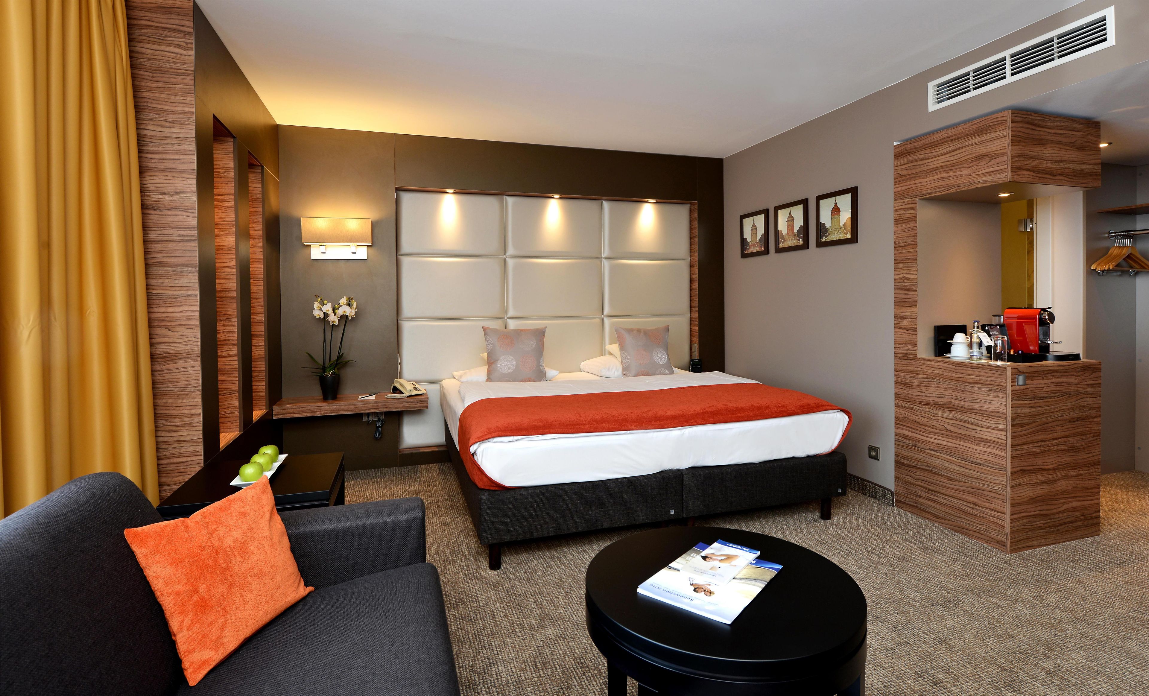 A hotel room with a bed, a sofa, a coffee machine, and a small table with magazines.