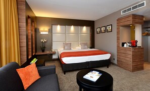 Habitación de hotel con cama, sofá, cafetera y una pequeña mesa con revistas.