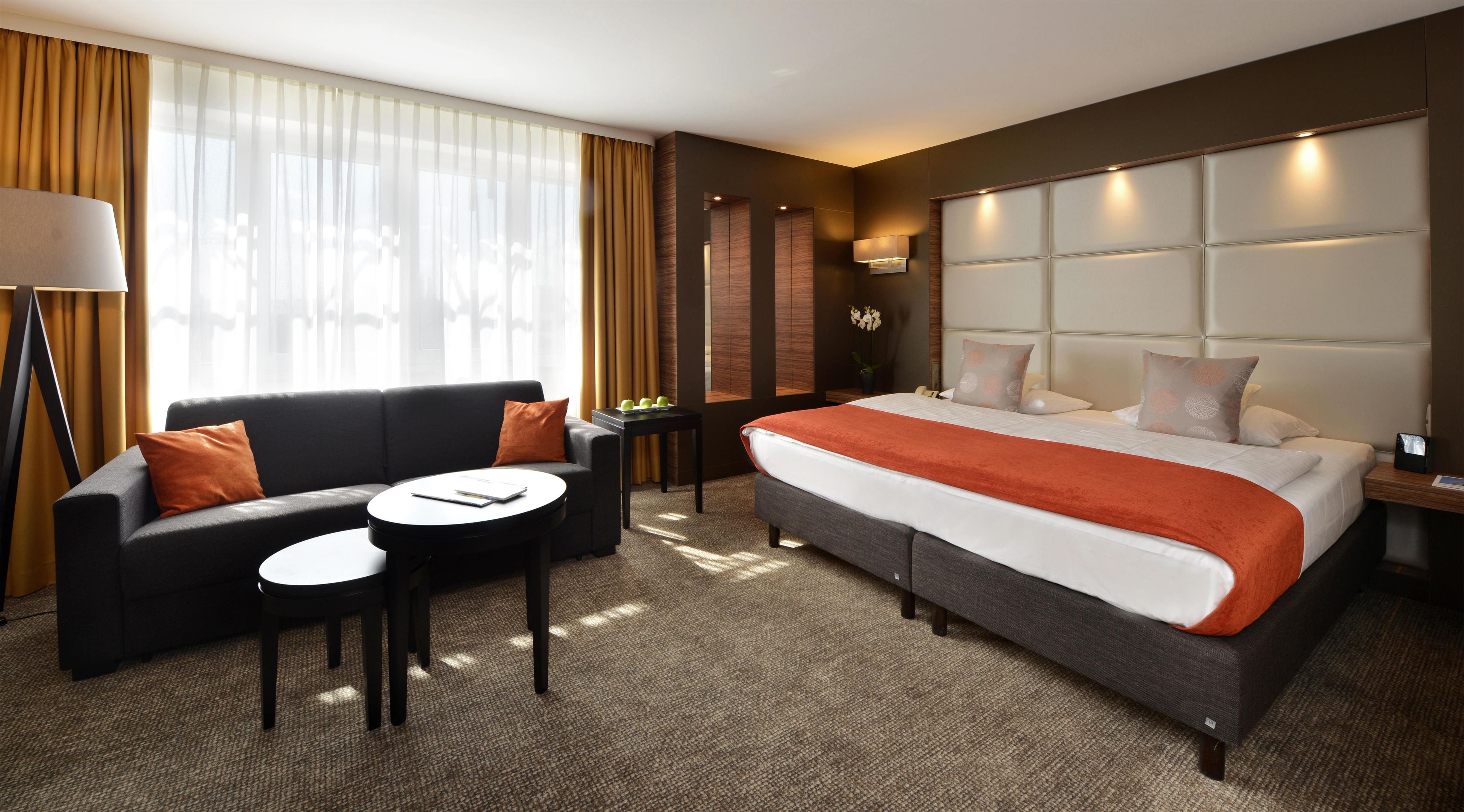 A hotel room with a bed, a sofa, a small table, and a lamp.
