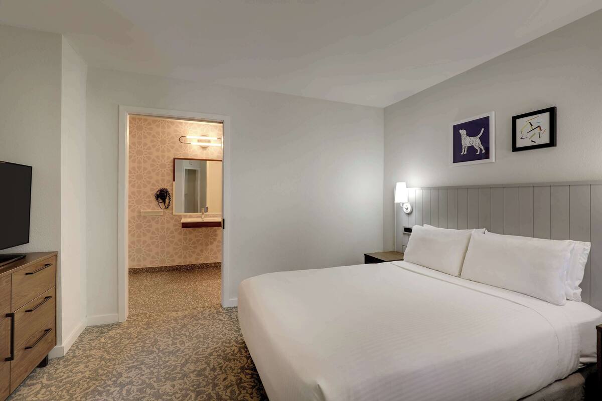 Ett hotellrum med en stor säng, en byrå, en tv och ett badrum som syns genom en öppen dörr.
