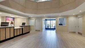 A spacious lobby with a reception desk, a staircase, and a view of the outside.