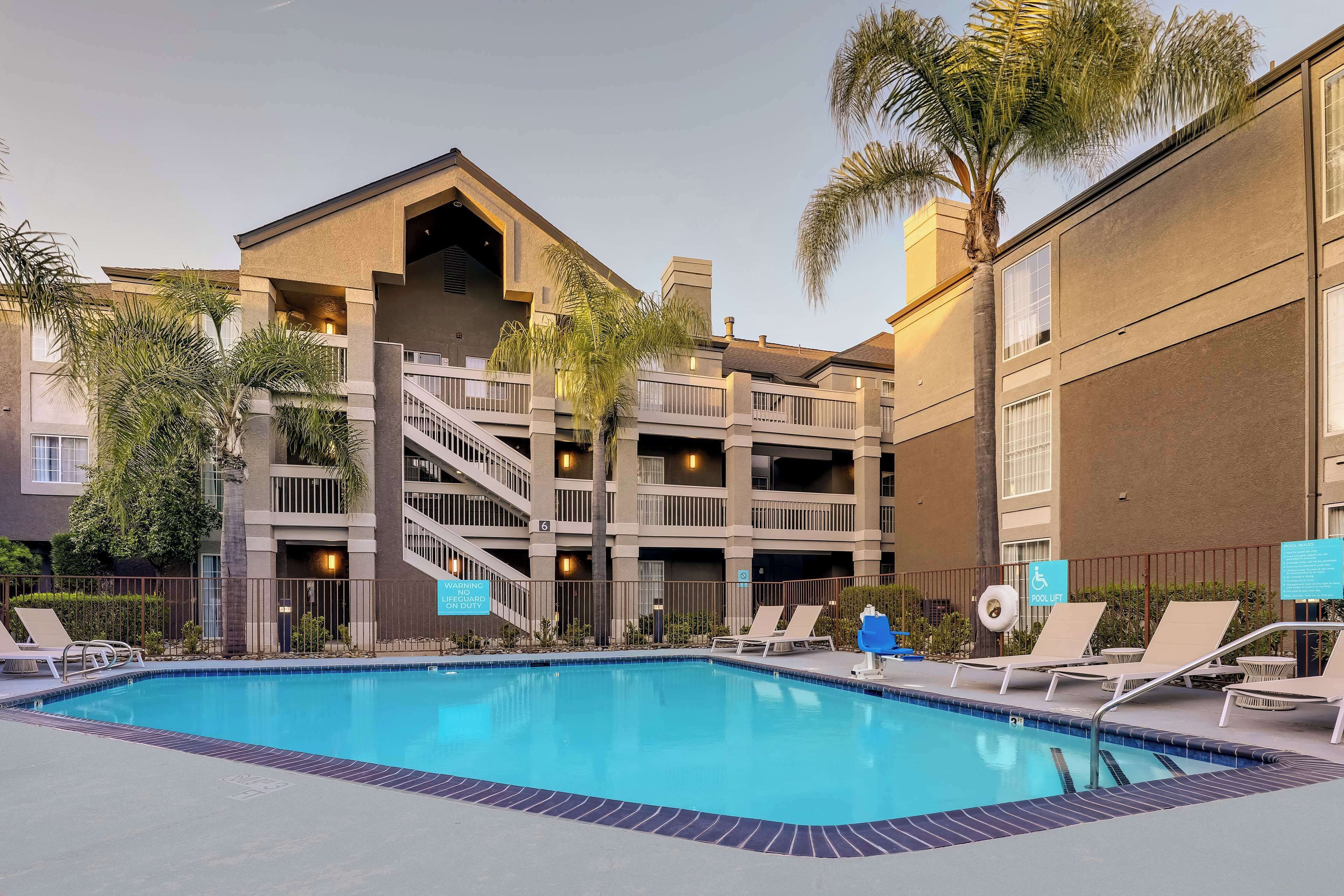 A hotel pool area with a clear view of the pool, lounge chairs, and a staircase leading to the upper floors.