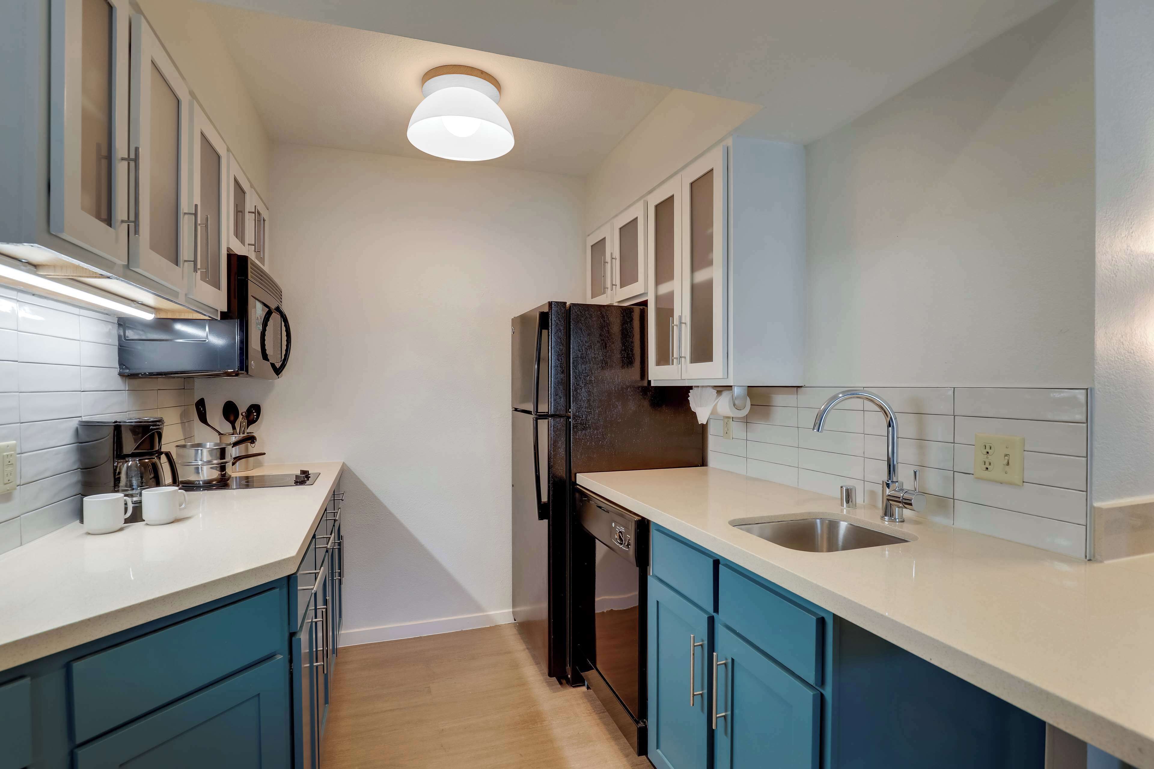 A compact kitchen with white and blue cabinets, a stainless steel sink, and a black refrigerator.