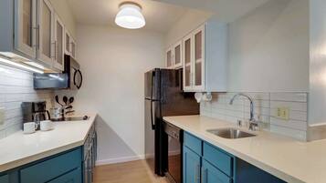 A compact kitchen with white and blue cabinets, a stainless steel sink, and a black refrigerator.