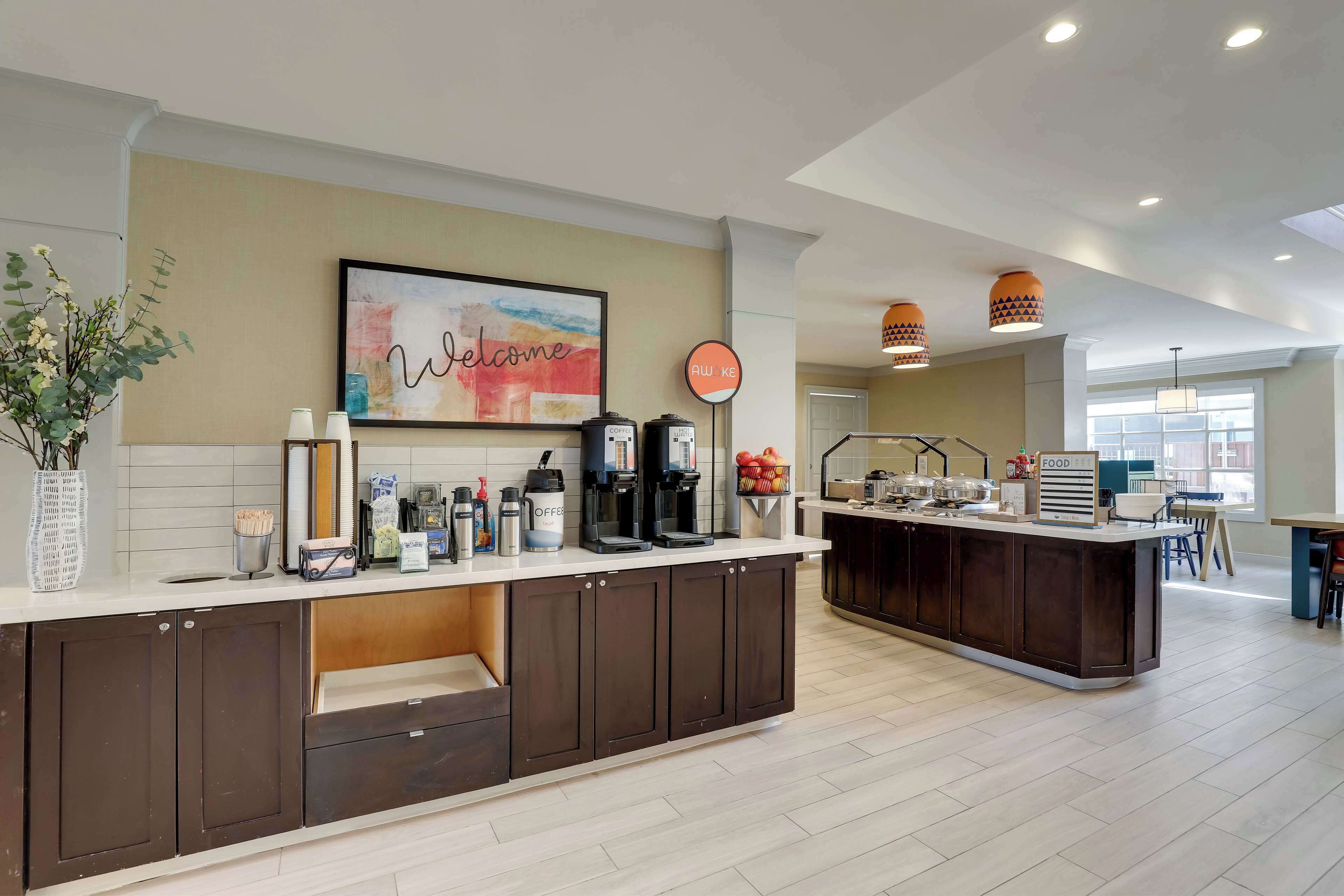 A modern kitchen with a central island, a welcome sign, and a coffee station.