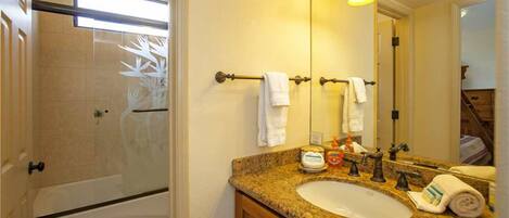 A bathroom with a granite countertop sink, a large mirror, and a shower area.