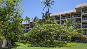 A hotel with multiple floors, balconies, and lush greenery including palm trees and flowering plants. - Kihei Akahi - Maui Condo & Home (Kihei)
