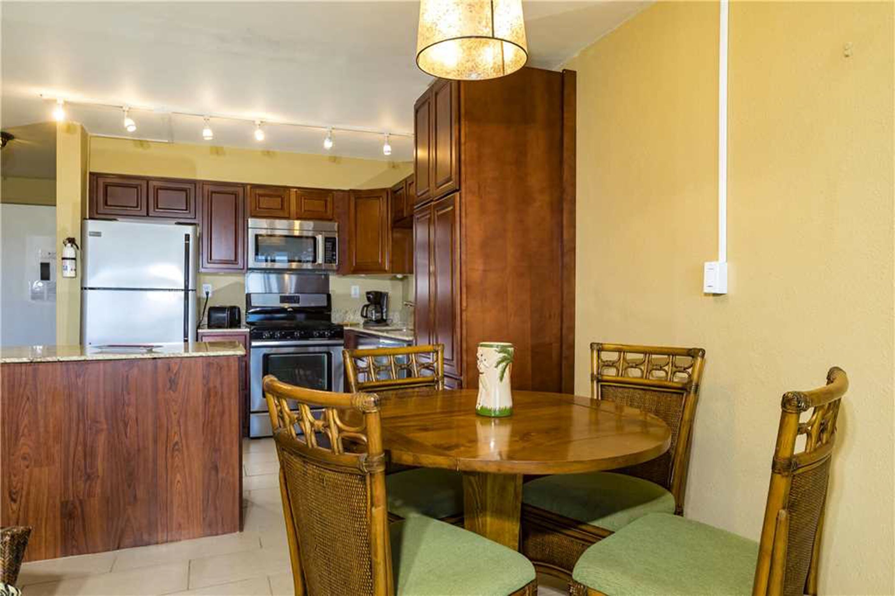 A kitchen with wooden cabinets, a stainless steel refrigerator, a microwave, and a stove. There is a dining table with four chairs.