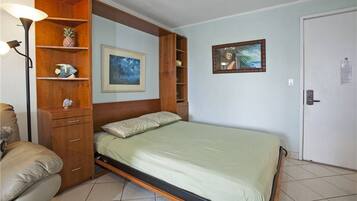 A single-bed room with a wooden headboard, a bedside lamp, a small shelf with a pineapple, and a framed picture on the wall.