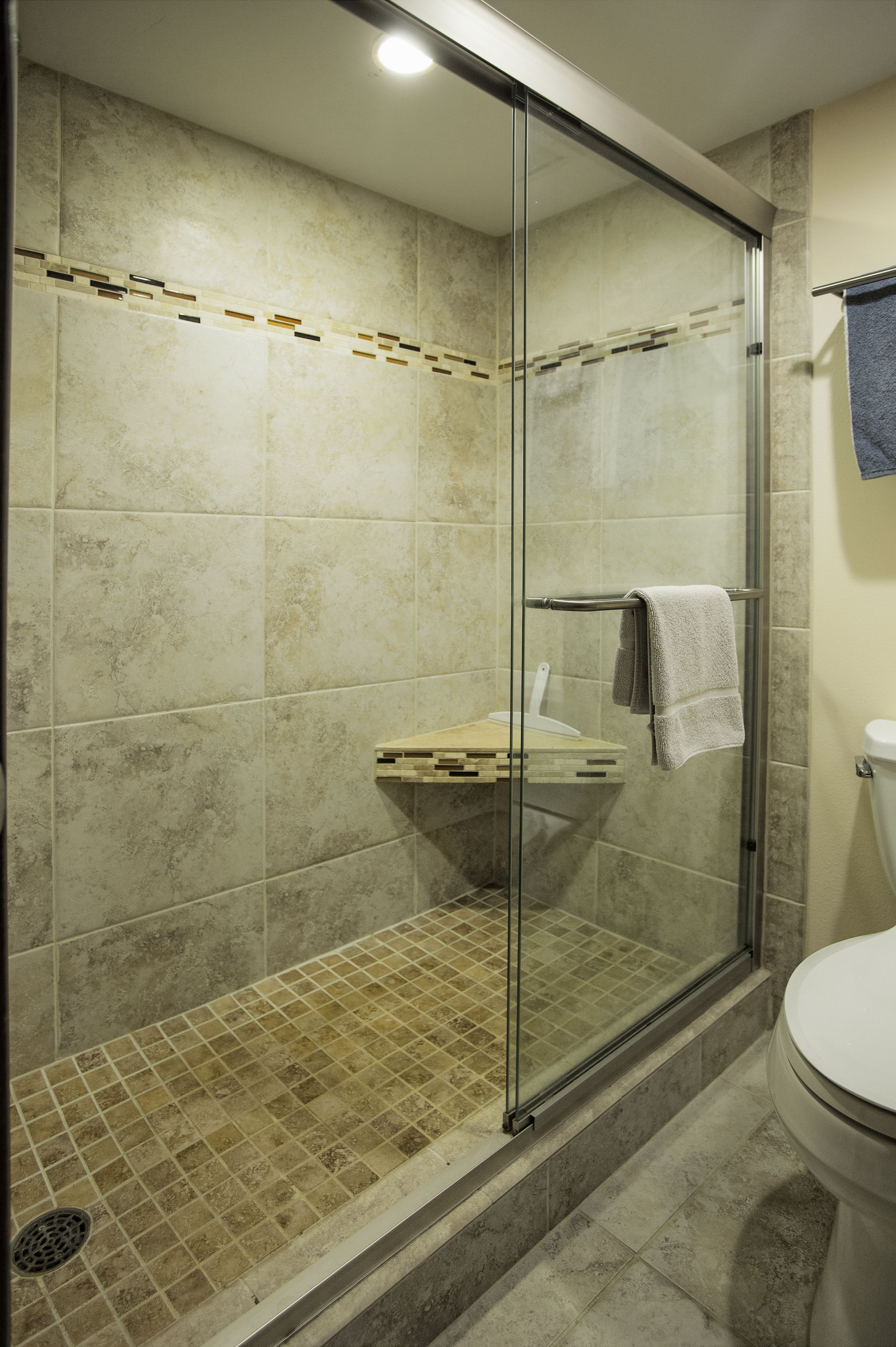 Une douche fermée par des parois de verre, avec un sol carrelé et un petit coin lavabo.