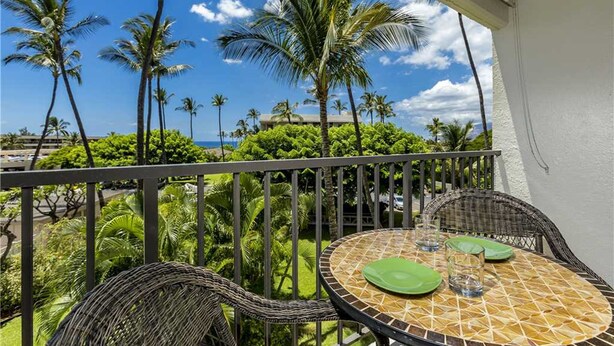 A balcony with wicker chairs and a round table, overlooking a lush garden and palm trees. - Kihei Akahi - Maui Condo & Home (Kihei)